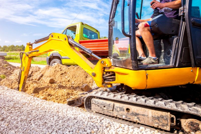 yellow excavator moving earth next to a road